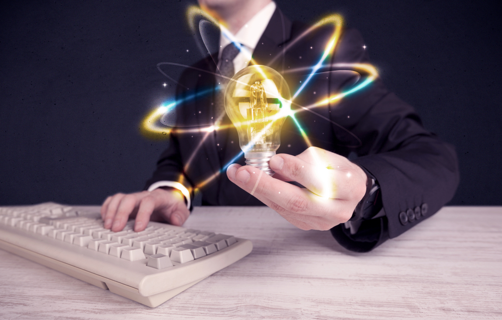 A classy businessman holding a colorful light bulb with shining circles in front of dark background concept.