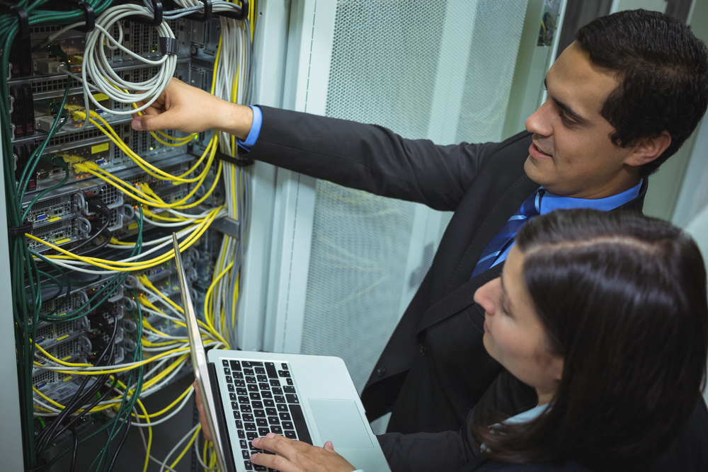 Technicians using laptop while analyzing server in server room